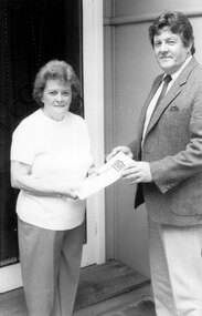 A man in a suit presenting an award to a woman more casually dressed.