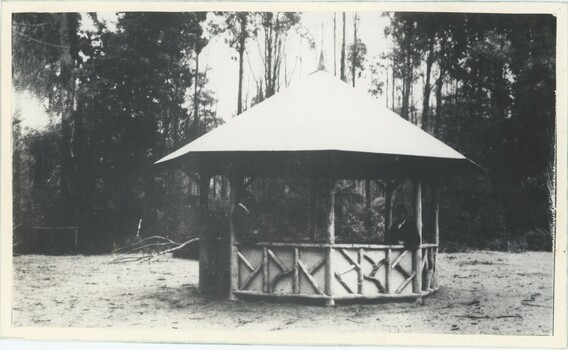 A black and white photograph of a rotunda on flat open ground, with trees in the background.