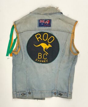 Image depicts the back of a sleeveless denim jacket, with yellow ribbon trim around the sleeve holes, a green and yellow ribbon off one shoulder, and a large back patch for 'Roo B.C. Sydney', the Roo Bike Club.