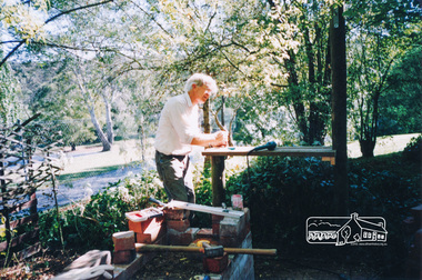 Photograph, Harry Gilham (Committee) building the BBQ grille near house, 1995