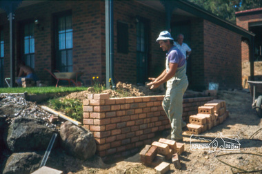 Photograph, Nick building brick wall along driveway, February 1982