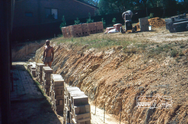Photograph, Peter Vermey standing on foundation for retaining wall on the back, February 1982