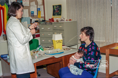 Photograph, Dianne Yans about to administer a vaccine shot to a young baby at the Maternal and Child Health Centre, War Memorial Hall, 905 Main Road, Eltham, 1989