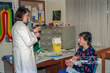Photograph, Dianne Yans about to administer a vaccine shot to a young baby at the Maternal and Child Health Centre, War Memorial Hall, 905 Main Road, Eltham, 1989