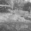 Children jumping on a pile of dirt which surrounds similiar sized piles of brick rubble at the rear of the car port.  VW Beetle is parked there.