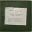 Large book of photographs with a hard, green cover which has 2 bolts holding the pages and cover together.