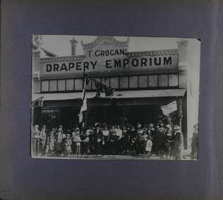 One photo of a crowd in front of a shop named as T Grogan's Drapery Emporium.  People are dressed in early 20th century clothes.