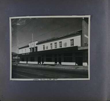 1 photo of of a long 2storey building with lots of doors and windows on a street with tram tracks.