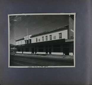 1 photo of of a long 2storey building with lots of doors and windows on a street with tram tracks.
