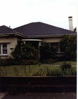 Partial view of a white house with brick features, semi circle porch entry, tall chimney.  View includes the front brick fence, garden path and garden.