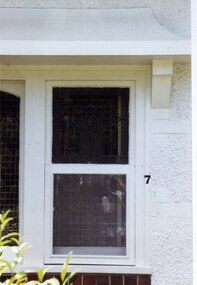 White-framed window amidst white wall, with a line of brown bricks underneath and a white ledge above. A few branches of a bush in the left foreground.