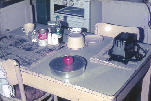 Kitchen table with toaster, delivered meal in round aluminium container with an apple on top.