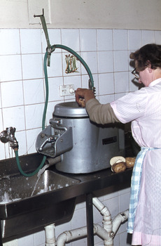 Women in an apron operating a commercial potato processing machine.