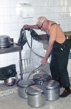 Kitchen worker spraying large aluminium round containers.