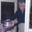 A women in an apron delivering a meal in an aluminium container to the hands of the recipient. 