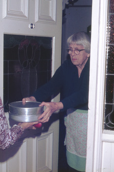 A women in an apron delivering a meal in an aluminium container to the hands of the recipient. 