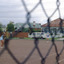 Two women playing tennis seen through a wire fence.