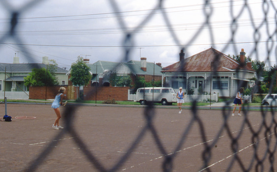 Two women playing tennis seen through a wire fence.
