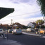 A T intersection with shop awning seen in the foreground and a number of parked cars and cars travelling along the road.