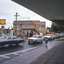 Shell service station on corner of T intersection with cars in the foreground along the road.