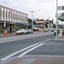 Shopping strip beside a T intersection with parked cars and a tram in the distance.