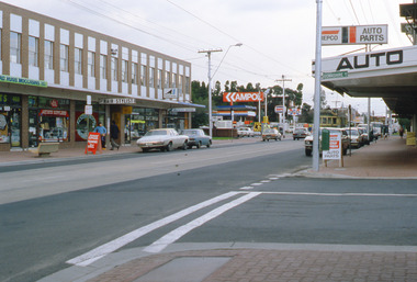 Shopping strip beside a T intersection with parked cars and a tram in the distance.