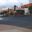 Shopping strip with pedestrian crossing and lights with a curved low brick fence in the foreground.