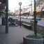 Looking  along shopping strip with a black sculpture and white ball lights on metal poles on paved area in the  foreground.