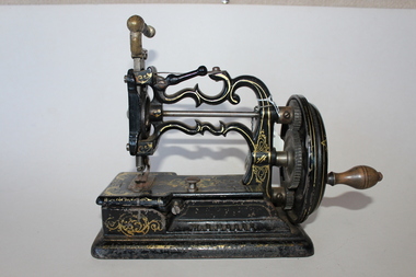Early sewing machine with hand cranking wheel; black with gold guilding