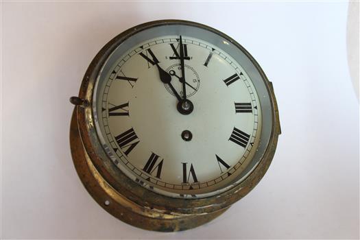 Clock with white face and roman numerals, showing tarnished brass housing.