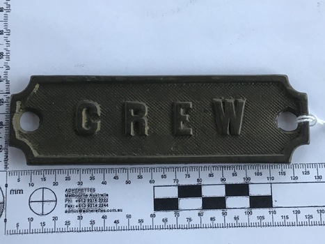 Small rectangular cast brass plate with 'CREW' inscribed in raised lettering over scribed background with scalloped corners containing two screw holes in ends