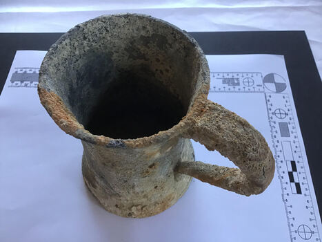 Top and side views of a heavily encrusted pewter tankard with a glass base.