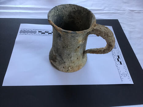 Top and side views of a heavily encrusted pewter tankard with a glass base.