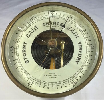 A brass barometer with white face. 