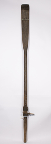 A timber oar with fitted metal rowlocks which has a lower metal strap across the blade attached. The top strap is missing.