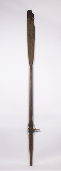 A timber oar with fitted metal rowlocks which has a damaged blade with the top strap still attached. The lower strap is missing.