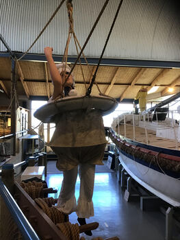 Life saving buoy with canvas breeches suspended by 4 ropes to pulley system with a pull rope used to haul survivors ship to ship or ship to shore 