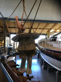 Life saving buoy with canvas breeches suspended by 4 ropes to pulley system with a pull rope used to haul survivors ship to ship or ship to shore 