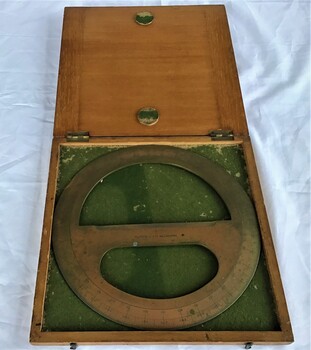 A brass drawing circle protractor in a flat, square wooden box lined with green felt and brass fittings.