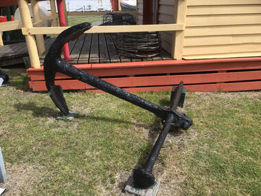 Admiralty type anchor painted black containing a shaft with two fluked arms at bottom end and a stock and shackle at the top end. The stock at the top ensures that anchor flukes will bite into the bottom of the sea bed when the anchor is dragging due to current. 