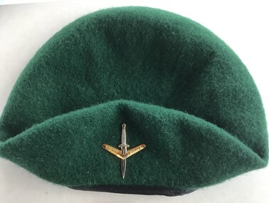 Green beret with badge consisting of silver dagger through gold boomerang inscribed with "Strike Swiftly"