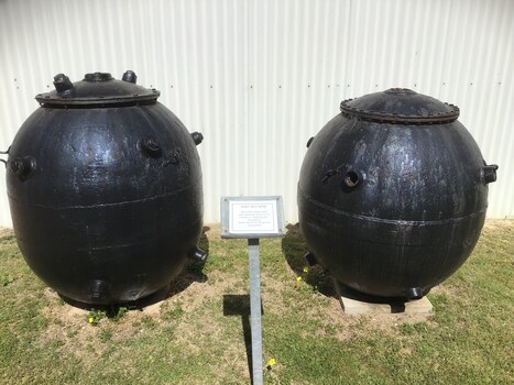 Two elongated oval shaped navy mines painted black. One showing bottom end and the other the top end. Each one has fuse connection points on the outside skin which operated the magnetic trigger devices. 