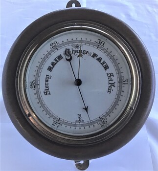 Aneroid barometer with white face and black lettering in round brass case fitted onto a timber base