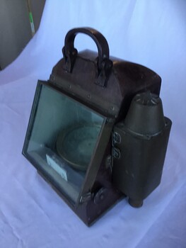 Portable compass in metal case with glass front and spirit light compartment on left side.