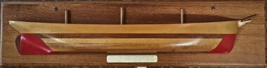 Half model of a nameless three masted sailing ship made of polished timber with red hull and three half masts. It is mounted on a timber back board with an inscription beneath.