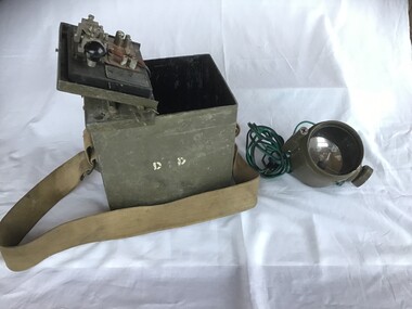 Two views showing a World War two Morse and day signal light set in timber box with webbing strap. A metal box containing spare globes and copper connectors. 