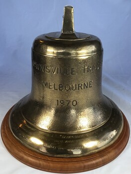 A brass ship's bell from the MV Townsville Trader mounted on a timber base.