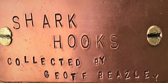 Label screwed onto display board containing four shark hooks