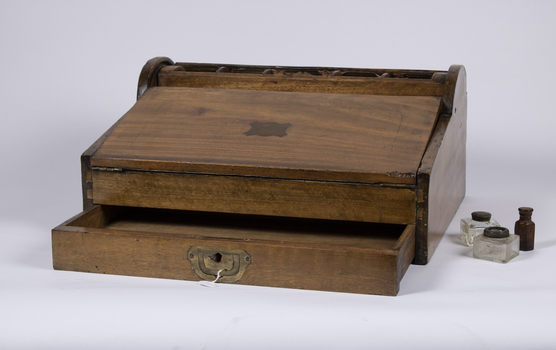 A mahogany lap writing desk with roll top lid shown in the closed position and an open drawer.