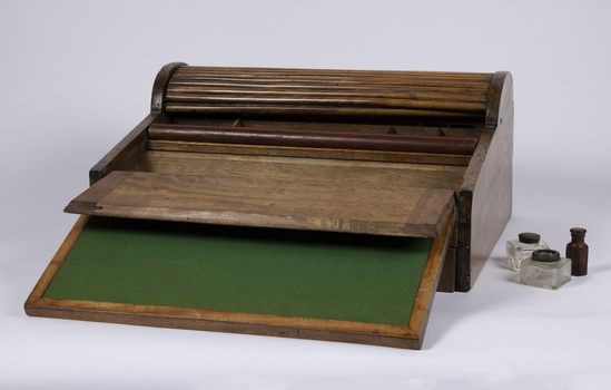 A mahogany lap writing desk with roll top lid shown in the open position and an open compartment and contents.